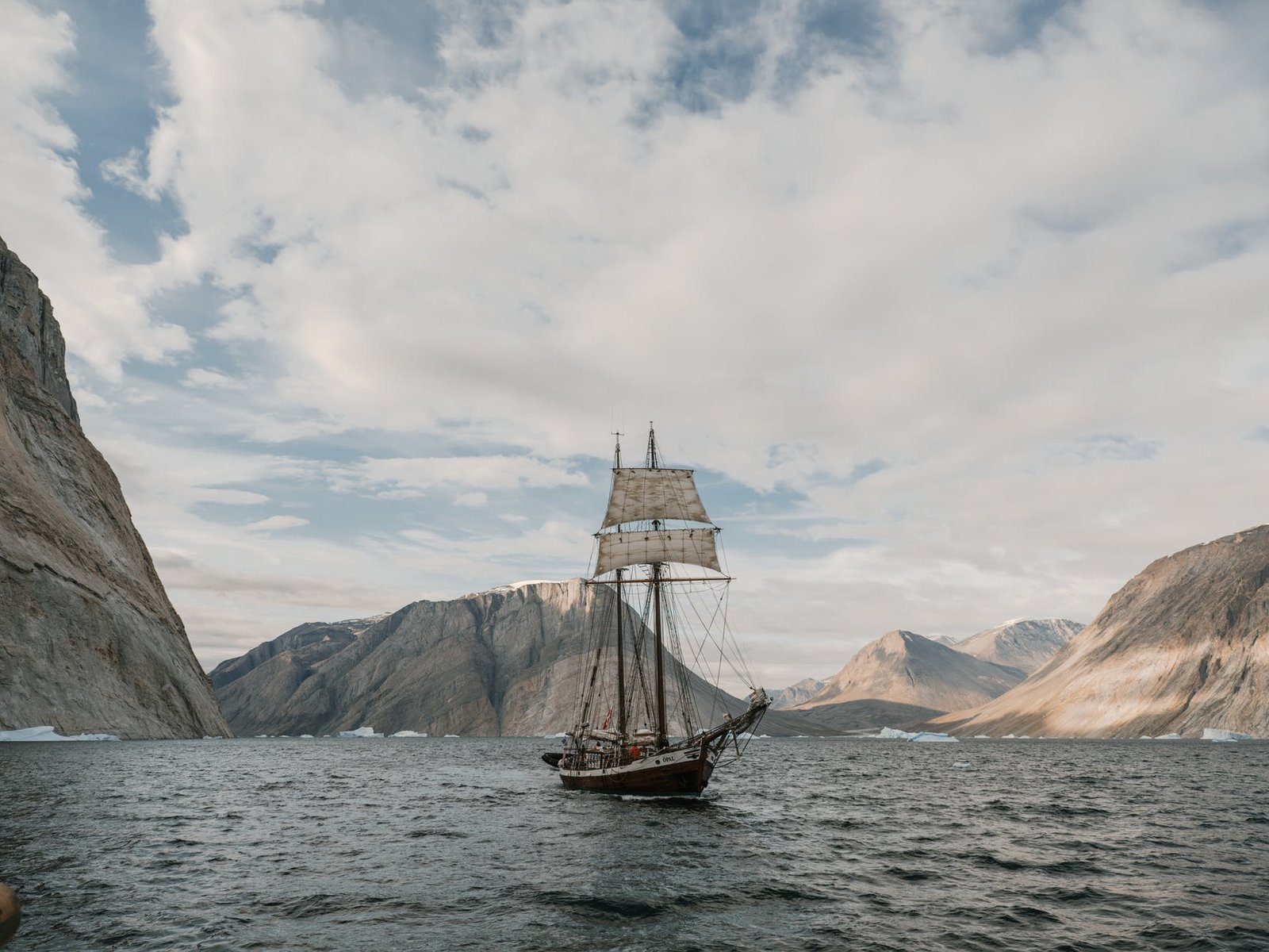 brown boat on sea near brown mountains under gray clouds